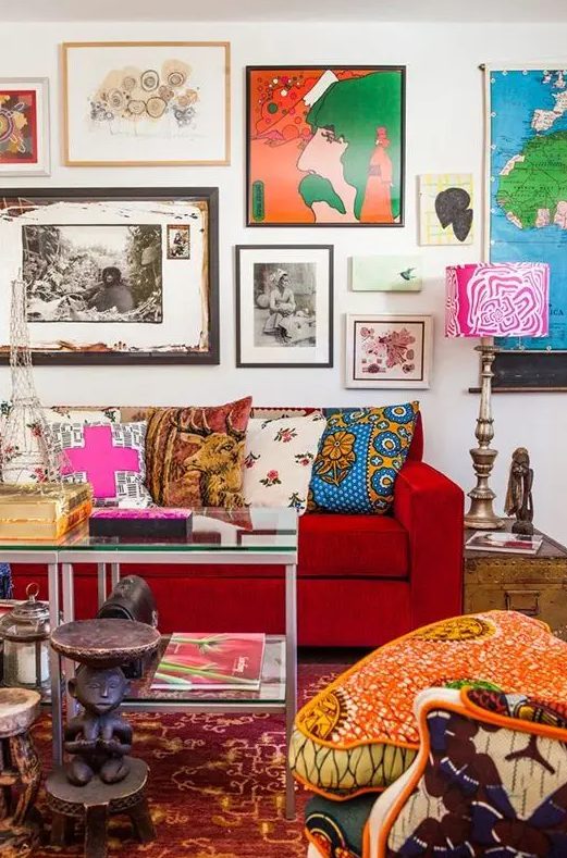 a maximalist living room with a colorful gallery wall, a hot red sofa, a printed chair, a bright rug and some pillows and books