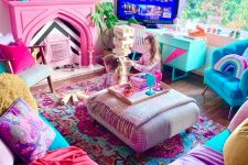 a maximalist living room with a pink fireplace, a turquoise sofa with colorful pillows, a mint TV unit and a bright rug is wow