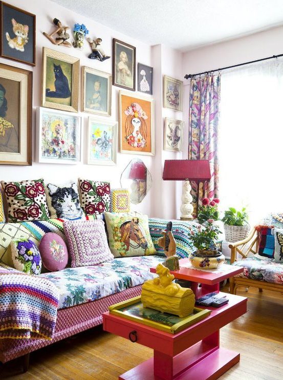 a maximalist living room with a pink sofa, table and lamp, a colorful gallery wall, bold upholstery and pillows plus various plants