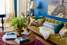 a maximalist living room with navy walls, a fuchsia printed rug, a mustard sofa and blue chairs and a bold artwork