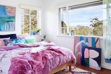 a maximalist ocean bedroom with simple furniture, colorful bedding and a bold artwork plus a gorgeous view