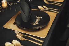 a minimal black and gold party table with gold placemats and cutlery, gold candleholders and black napkins is wow
