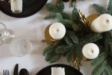 a modern and stylish Christmas tablescape with black plates and chargers, black cutlery, gold foliage and candleholders and fir branches