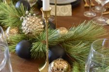 a modern black and gold Christmas table runner with evergreens, black and gold ornaments and candles dotting the table