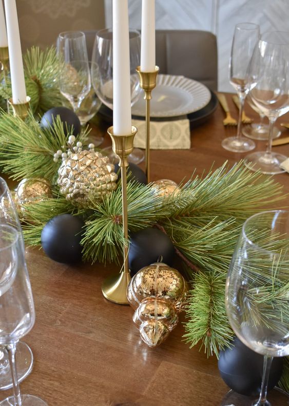 a modern black and gold Christmas table runner with evergreens, black and gold ornaments and candles dotting the table