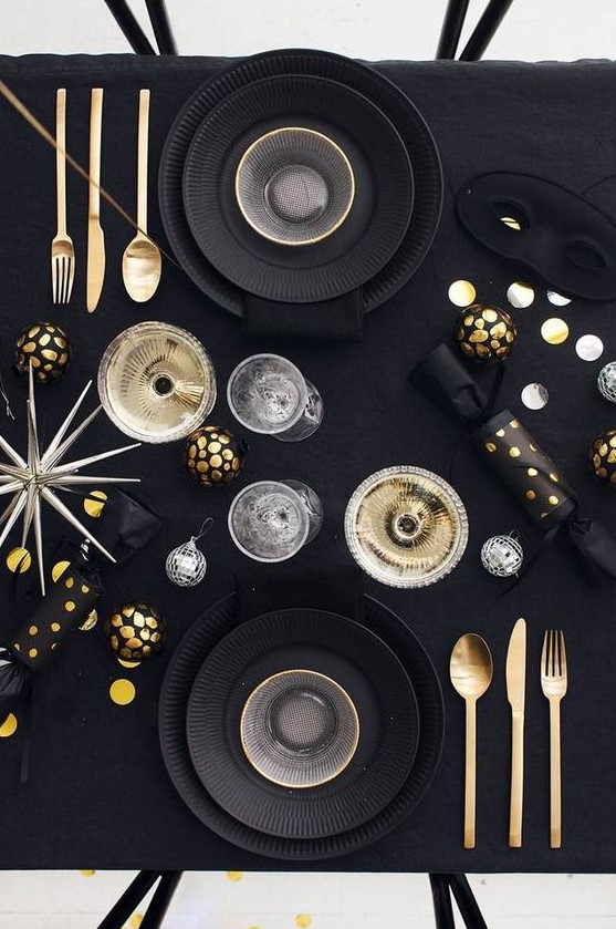 a modern black and gold party tablescape with black plates, gold and black ornaments, a large star and disco balls