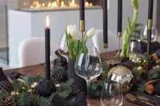 a modern holiday table with gold charger, cutlery, black and shiny ornaments, black candles and white blooms plus bells