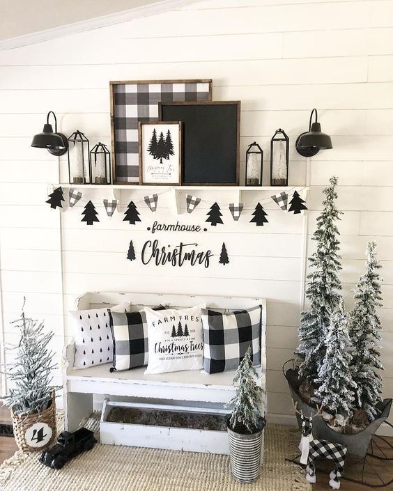 a pretty black and white Christmas entryway with a white bench, a shelf with signs, lanterns, a Christmas tree banner and snowy Christmas trees