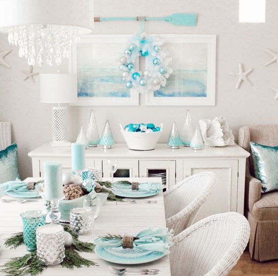 a pretty coastal Christmas space with aqua-colored porcelain, candles and candleholders, evergreens, a white wreath with white and aqua ornaments and coastal artworks