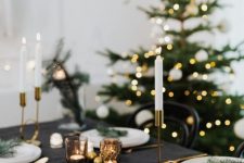 a pretty modern Christmas tablescape with black linens, candles in gold candelholders, white plates and gold cutlery
