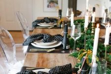 a pretty tablescape with black placemats and printed black napkins, a greenery runner with LEd lights and champagne bottles