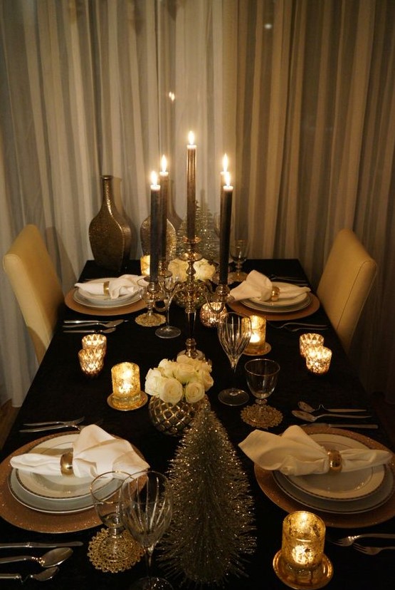 a refined black and gold party tablescape with white roses, a bottlebrush tree, black candles and white porcelain plus gold candleholders