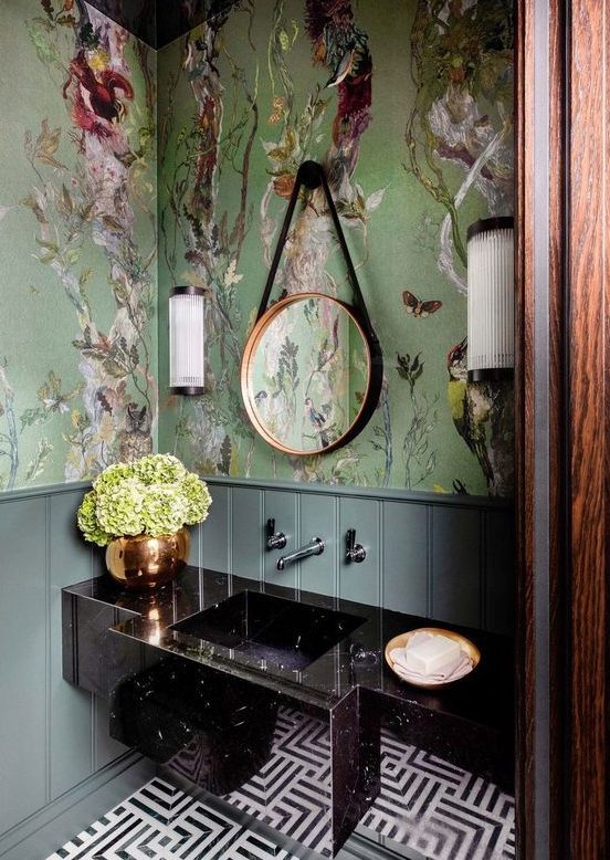 a refined maximalist bathroom with green flora and fauna wallpaper, a black stone vanity, a mosaic tile floor and a round mirror