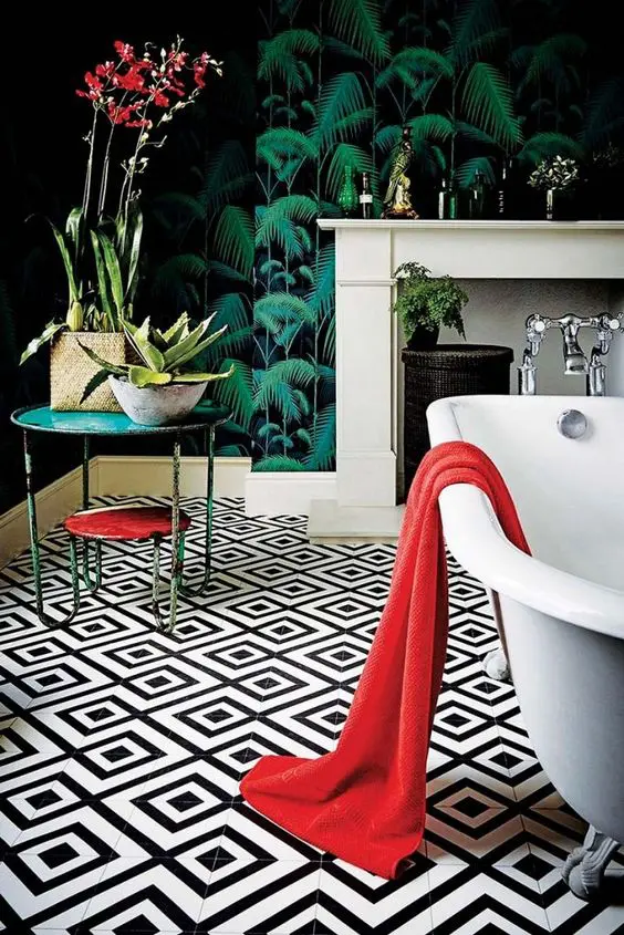 a refined maximalist bathroom with moody tropical wallpaper, black and white tiles on the floor, a clawfoot tub, coffee tables and a faux fireplace