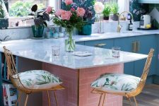 a refined maximalist kitchen with moody floral wallpaper walls, pale blue cabinets, a pink kitchen island with a white stone countertop and tall stools with printed cushions