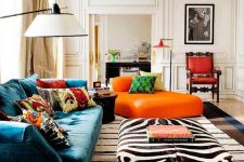 a refined maximalist living room with neutral paneled walls, a teal sofa and an orange lounger, a zebra ottoman, colorful pillows and rugs