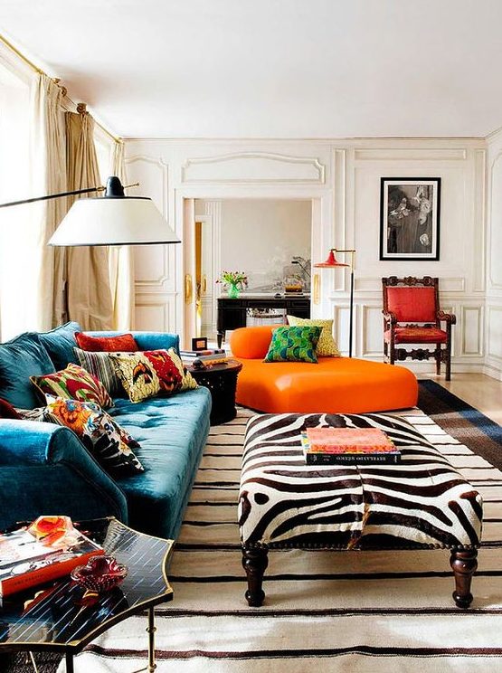 a refined maximalist living room with neutral paneled walls, a teal sofa and an orange lounger, a zebra ottoman, colorful pillows and rugs
