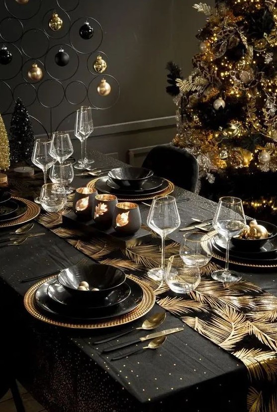 a shiny black and gold Christmas tablescape with leaves printed, gold chargers and black plates, candles and an ornament stand
