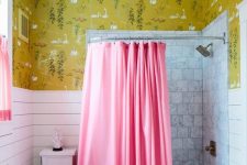 a stylish bathroom with bold mustard wallpaper, white paneling and marble tiles, pink curtains and a brass stool and fixtures just wows