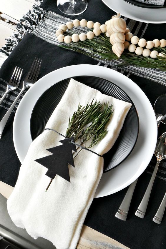 a stylish black and white Scandinavian Christmas tablescape with black and white linens, plates, greenery and wooden beads is amazing