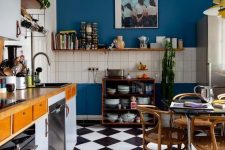 a stylish maximalist kitchen with bold blue walls, pale blue and stained cabinets, a checked floor and stained furniture