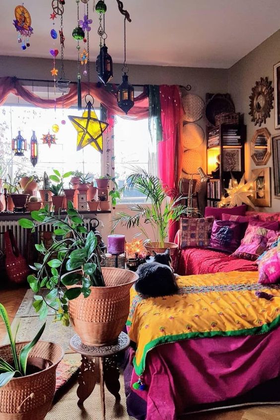 a super bright hippie bedroom with a red sofa and a fuchsia bed, colorful pillows and bedding, bright pendant lamps and curtains and lots of plants