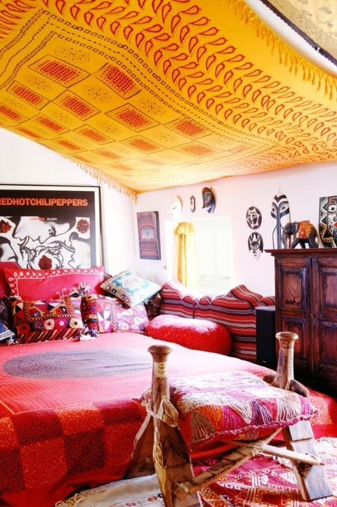 a super contrasting bedroom with a yellow printed ceiling, a red bed and a soft bench, a printed stool and some metallics