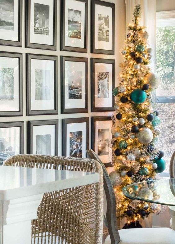a tall and thin Christmas tree with white, gold, silver, black ornaments and oversized teal ones is a stylish modern idea