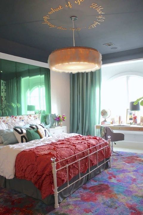 a tasteful maximalist bedroom with a shiny green accent wall, a white forged bed with bright bedding and a rug, a fluffy pendant lamp