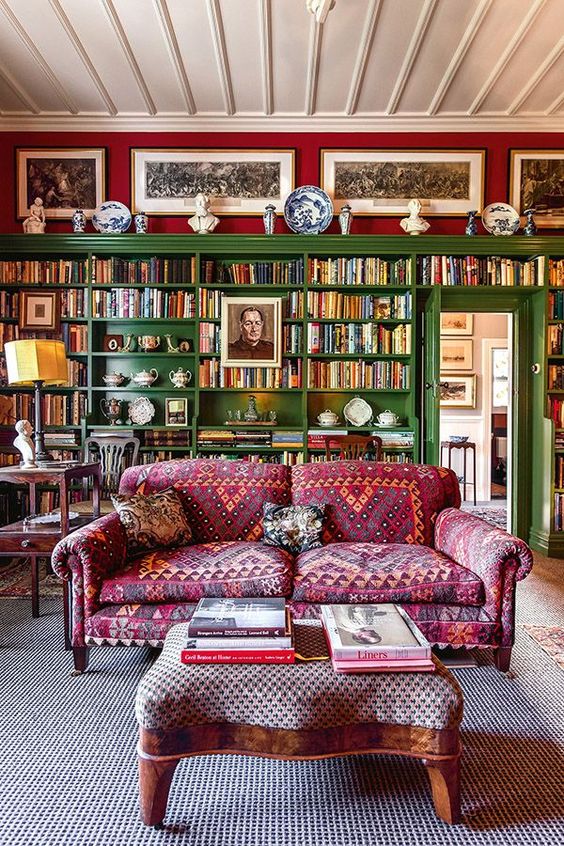 a vibrant maximalist library and home office with red walls, an oversized green built in bookcase, a pink printed sofa and lots of decor
