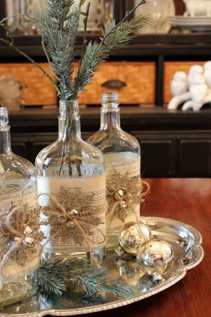 a vintage rustic Christmas centerpiece of a silver tray with fir twigs and silver ornaments, bottles with snowflakes and silver bells and fir twigs in them