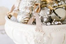 a vintage white bowl with silver and gold glitter Christmas ornaments and bells plus crystals and ribbons as a refined holiday centerpiece