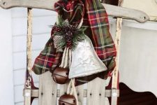a vintage wooden sledge with a plaid scarf, a porcelain bell ornament and some large brown bells for outdoor decor