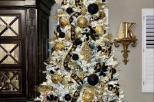 a white Christmas tree with black and gold ornaments, black and gold branches on top and some ribbon is amazing