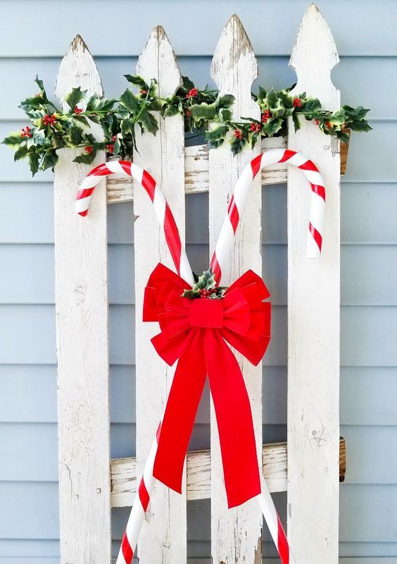 a white sleigh with candy canes and a red bow, greenery and berries on top for outdoor Christmas decor