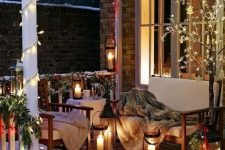 a winter terrace with a deck, elegant white outdoor furniture, faux fur blankets, candle lanterns, lights and evergreens is super cool