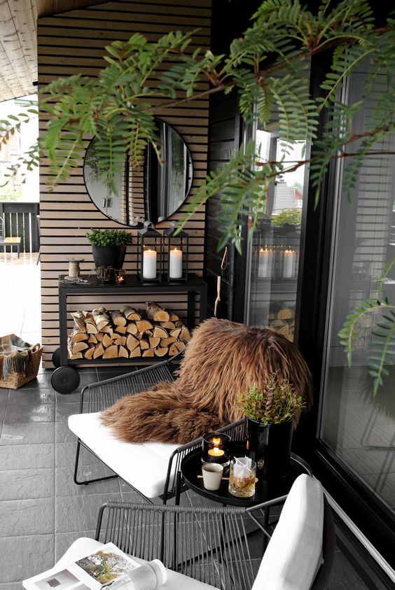 a winter terrace with metal white chairs, a black coffee table and a console, greenery, firewood and candle lanterns