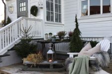a winter terrace with planked furniture, Christmas trees, a sledge with some grass and a candle lantern and some greenery in pots