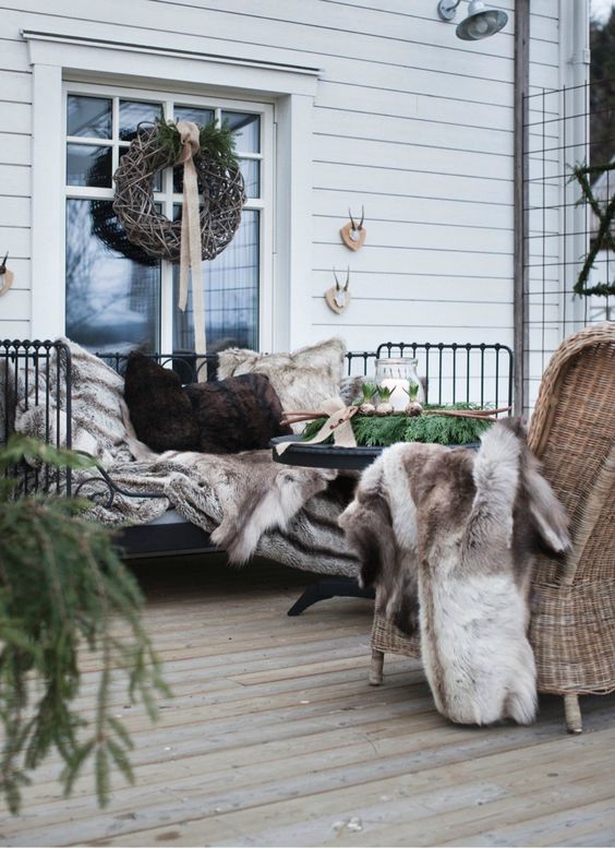 a woodland winter terrace with a forged daybed, a woven chair, faux fur, a vine wreath and some evergreens is a very welcoming space