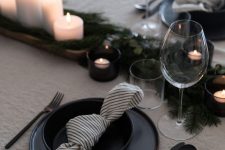 an elegant Scandi Christmas tablescape with pillar candles, evergreens, black plates and black cutlery is a very chic solution