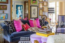 an elegant maximalist living room with a blue sofa, a lilac ottoman, white chairs, a fantastic gallery wall and lots of books and pillows