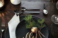 an elegant winter tablescape with black plates, bells with evergreens, bulbs in pots and candles