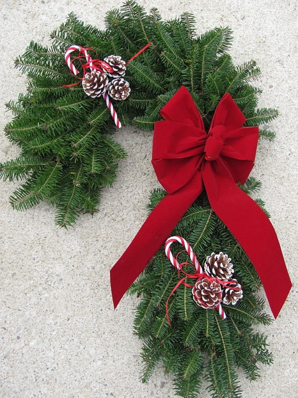 an evergreen candy cane shaped wreath with candy canes, snowy pinecones and an oversized red bow is a cool alternative to a usual wreath