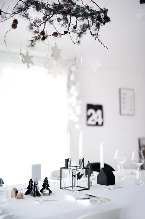 an ultra-minimalist Christmas tablescape with a black candelabra, white candles, black mini trees and a cool branch chandelier with clay snowflakes