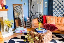 bright maximalist living room with blue walls, a chevron rug, an amber sofa and an ottoman, yellow chairs, a gold table and a fireplace