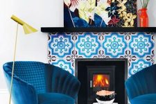 02 electric blue chairs, a bright blue printed rug, a bold blue tile fireplace and a colorful artwork create color galore
