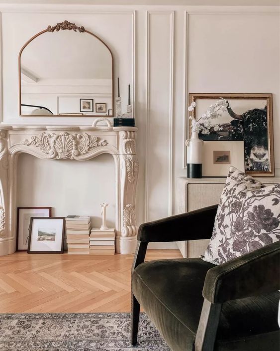 a beautiful and chic living room with a faux fireplace with an ornated mantel and books, with dark furniture and a large mirror