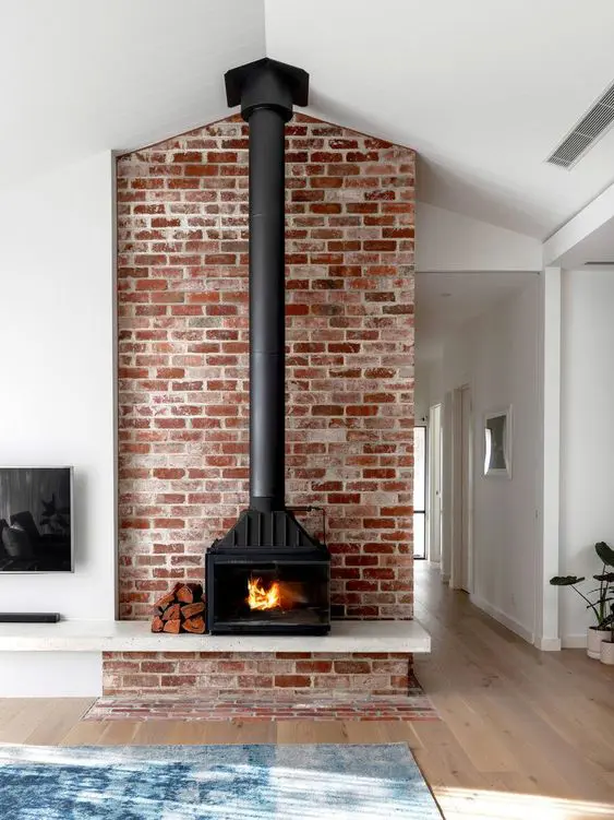 a black metal hearth surrounded with red brick and placed on a floating shelf for storing firewood here
