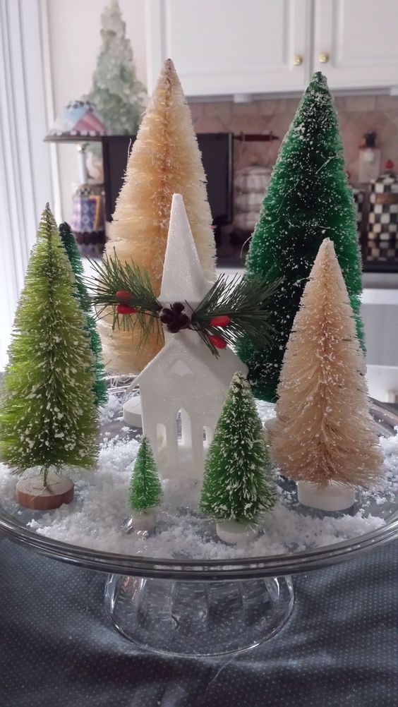 a glass stand with various bottle brush Christmas trees, a small white church and faux snow is a lovely centerpiece for a Christmas table
