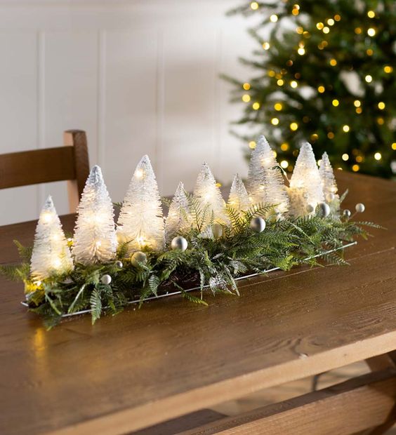 a lit up bottle brush Christmas tree centerpiece with ferns and silver ornaments is a fun and chic idea